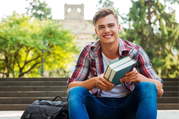 College student sitting on stairs smiling at camera.